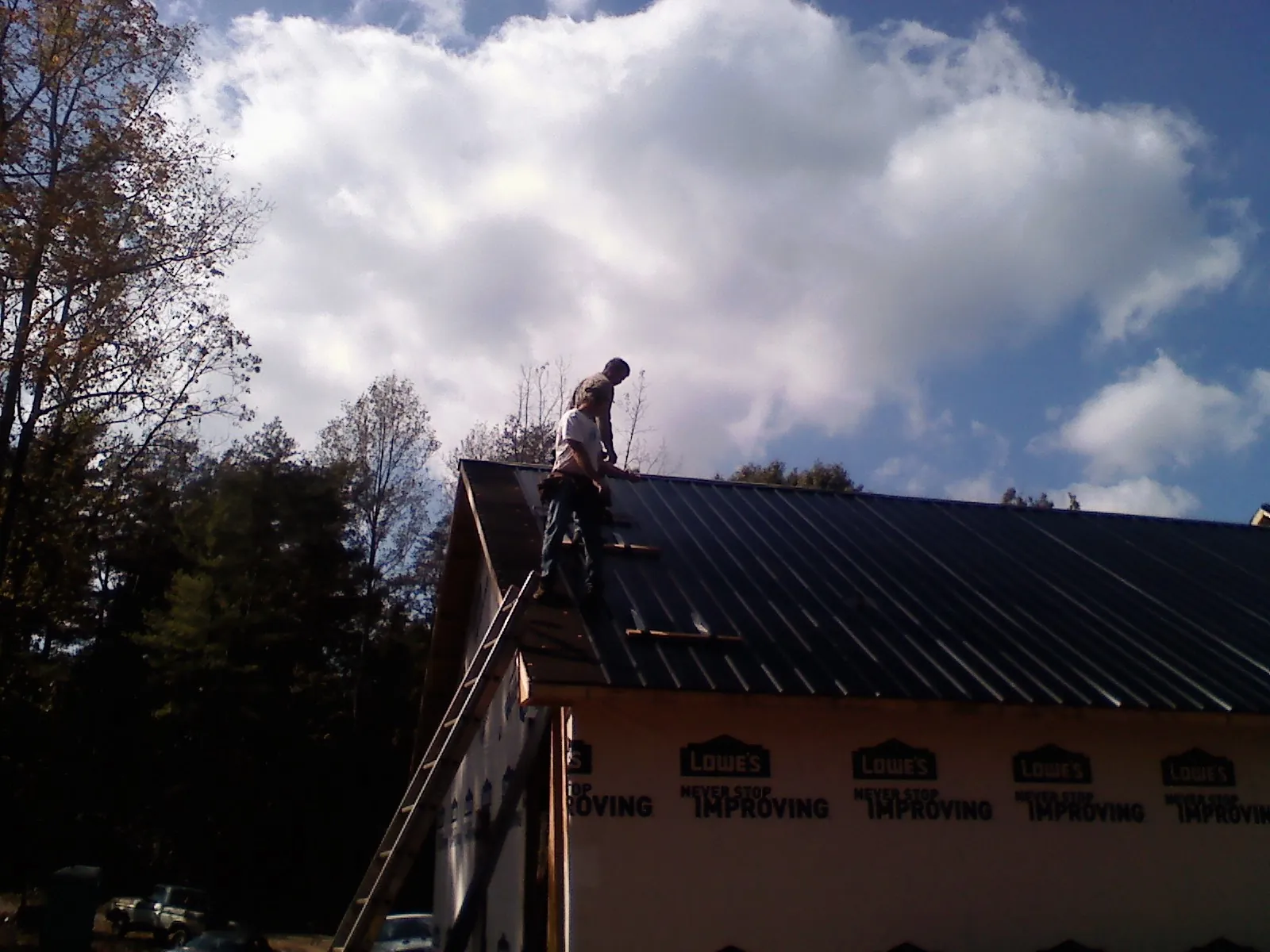 Roofer fastening dark metal panels high against a cloudy sky, from a Roof Inspection job in Corydon